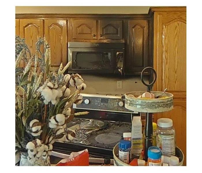 A kitchen where a black microwave has previously been on fire, now there is a black ring around the microwave