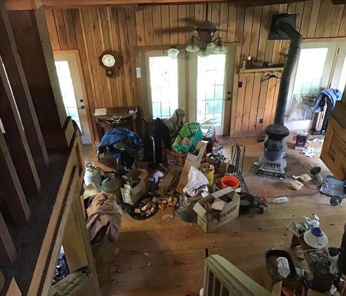 A log cabin home, looking down the stairs into the living room. The brown wood floor is covered is trash and dirt