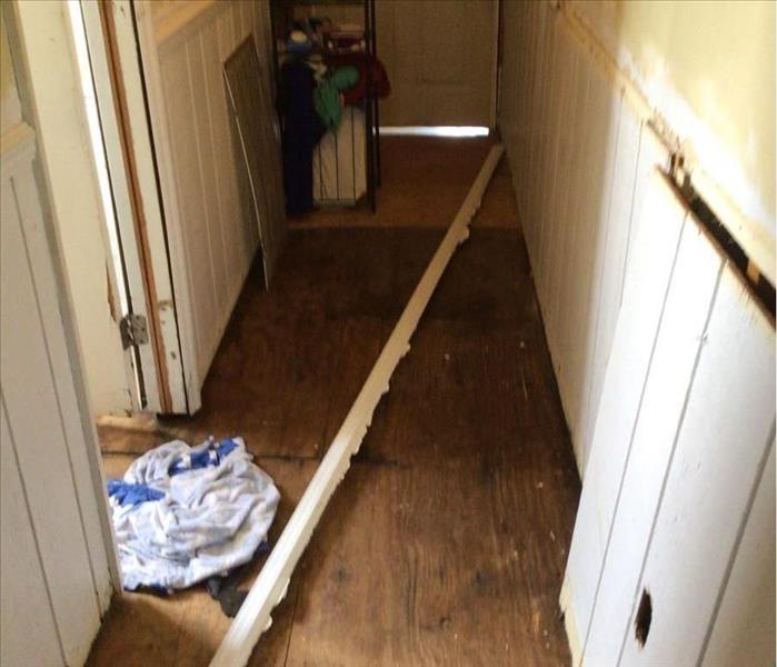 Looking down a hallway, hardwood floor has been removed, wooden subfloor is showing