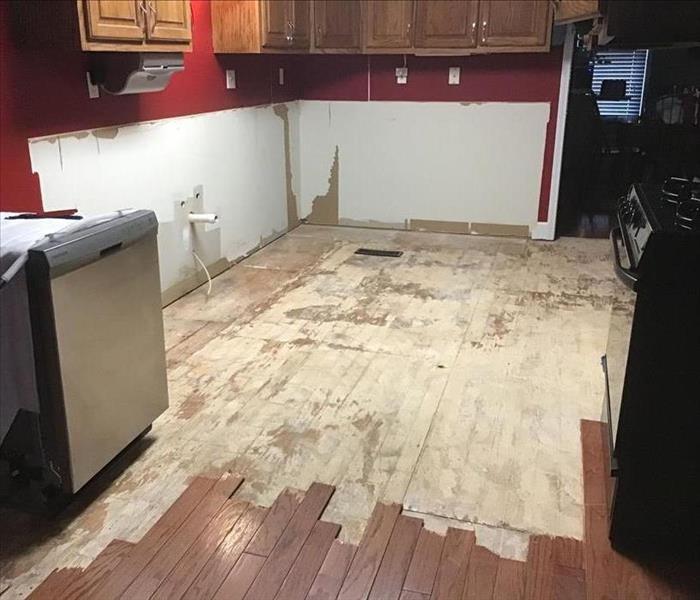A kitchen with red walls, wood flooring torn out, equipment has been moved, and kitchen appliances are in view