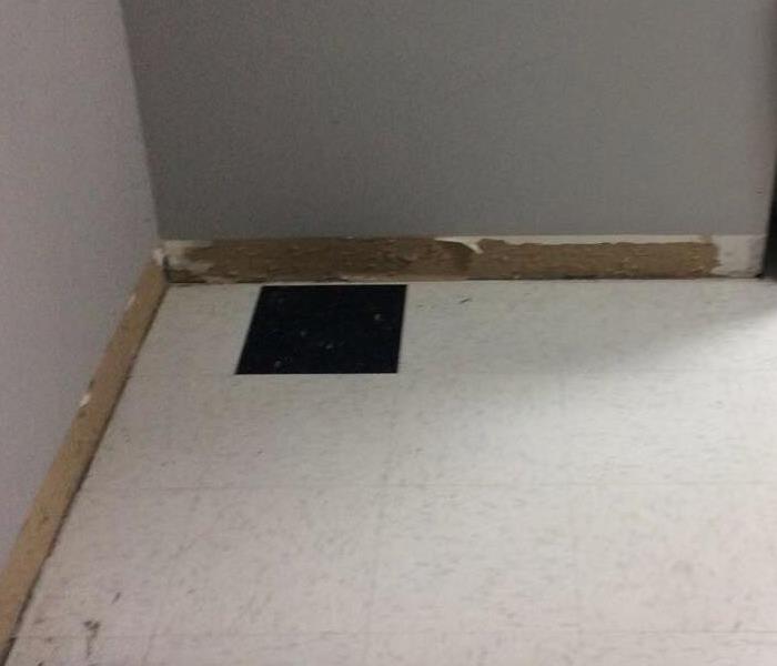 Wall in a school classroom that has the baseboards taken off with holes drilled in them