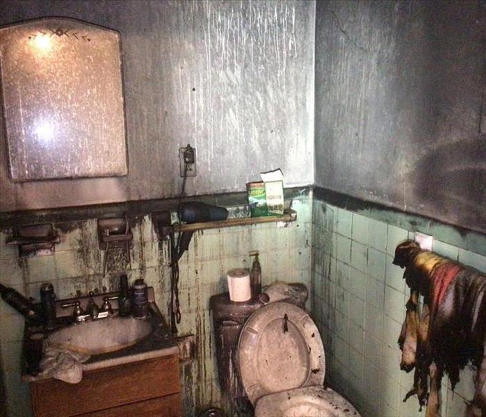 A bathroom that is completely affected by fire damage. There is gray soot on the walls, and a towel that has been burned 