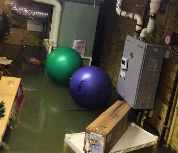 A flooded basement with visible standing water, two workout balls, and power box