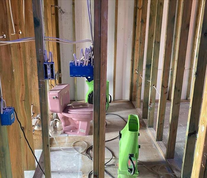 A shot of a bathroom in a home, with walls torn down to studs, and a pink toilet